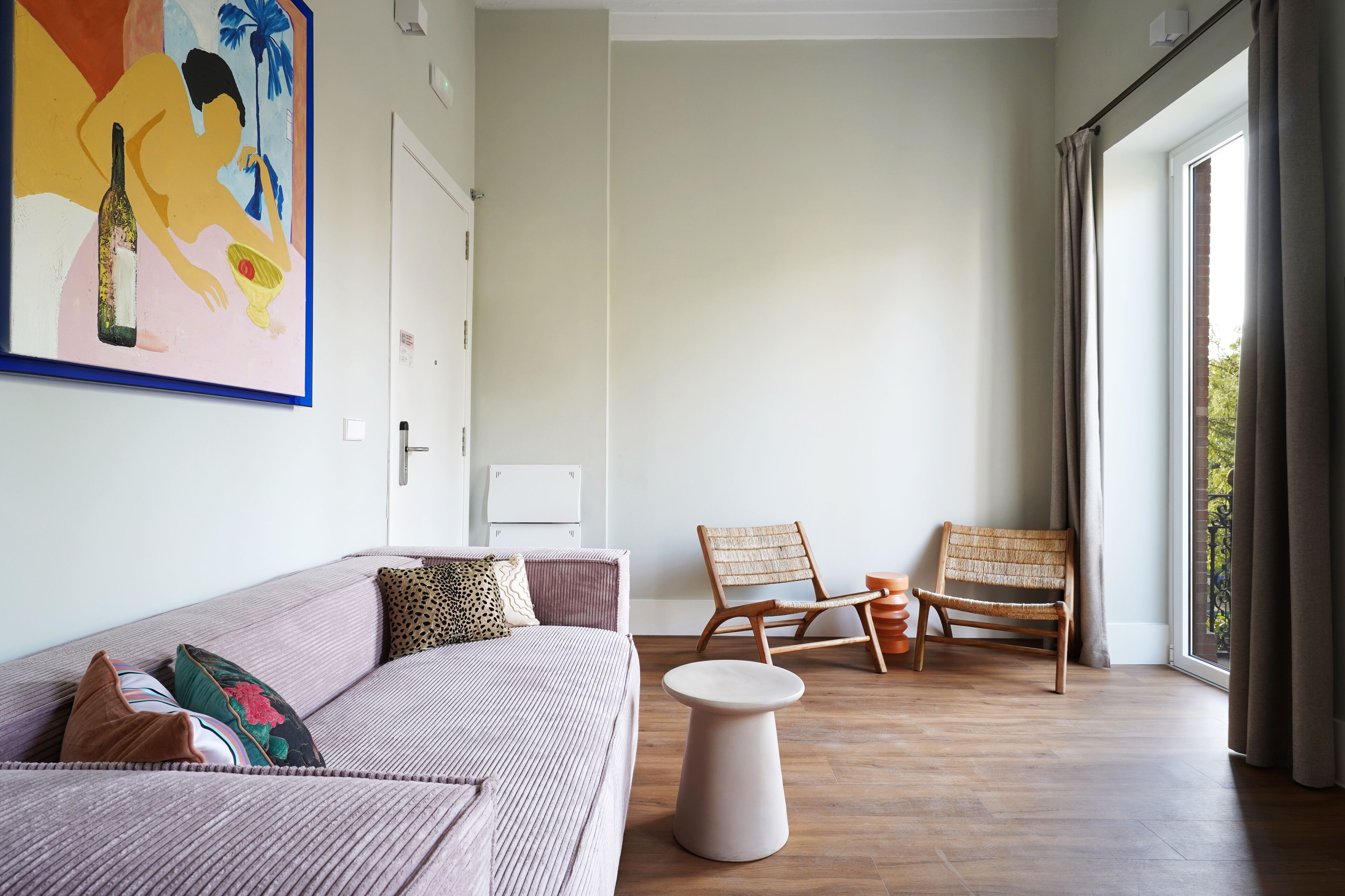 A modern living room with a sofa, two wicker chairs, a small round table, and a large window with curtains.