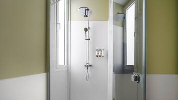 A glass-enclosed shower with a handheld showerhead and a wall-mounted showerhead. There are three bottles of shampoo and conditioner on the wall.