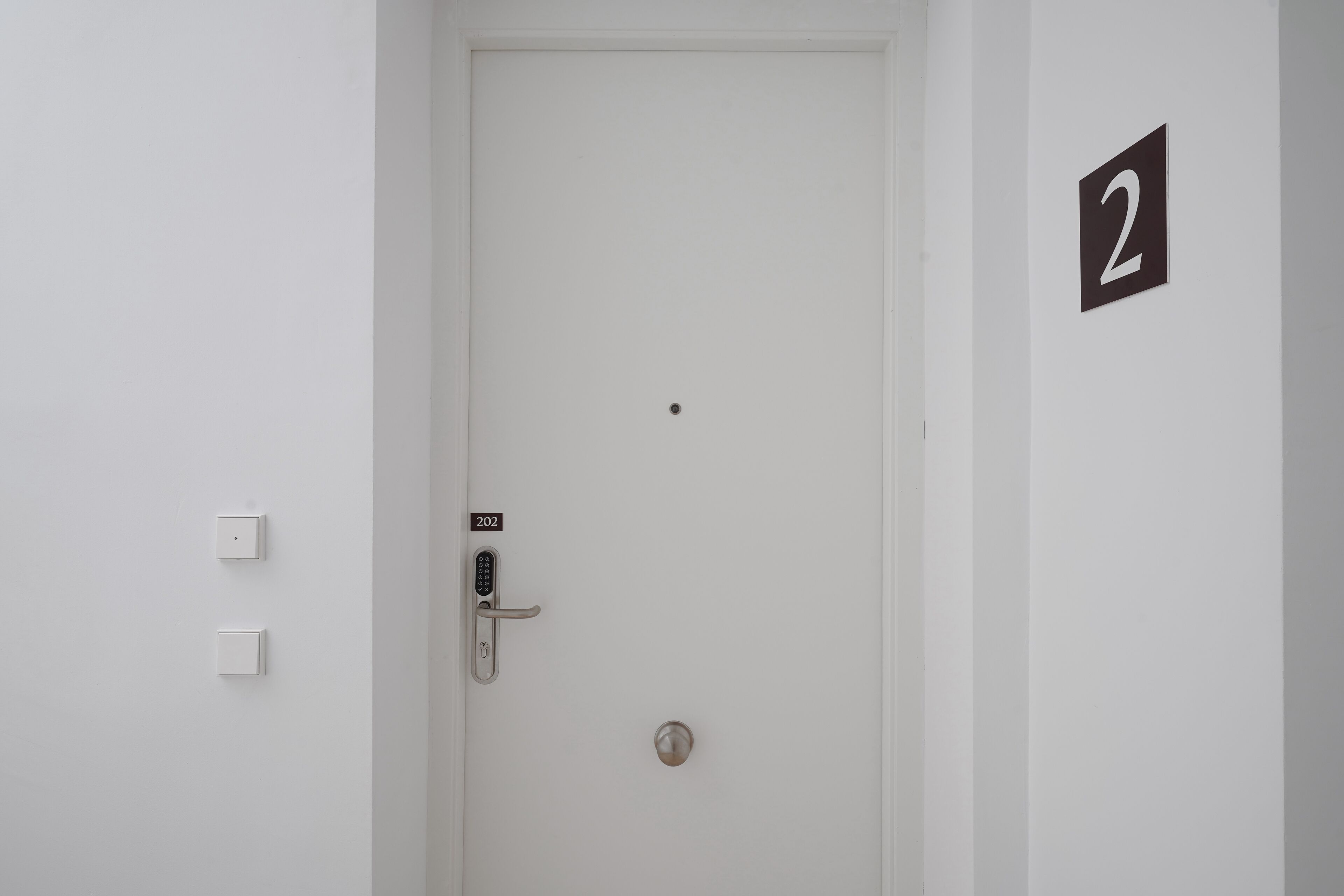 A white door with a numeric keypad lock, a doorbell, and a small number '2' sign on the wall.