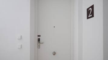 A white door with a numeric keypad lock, a doorbell, and a small number '2' sign on the wall.