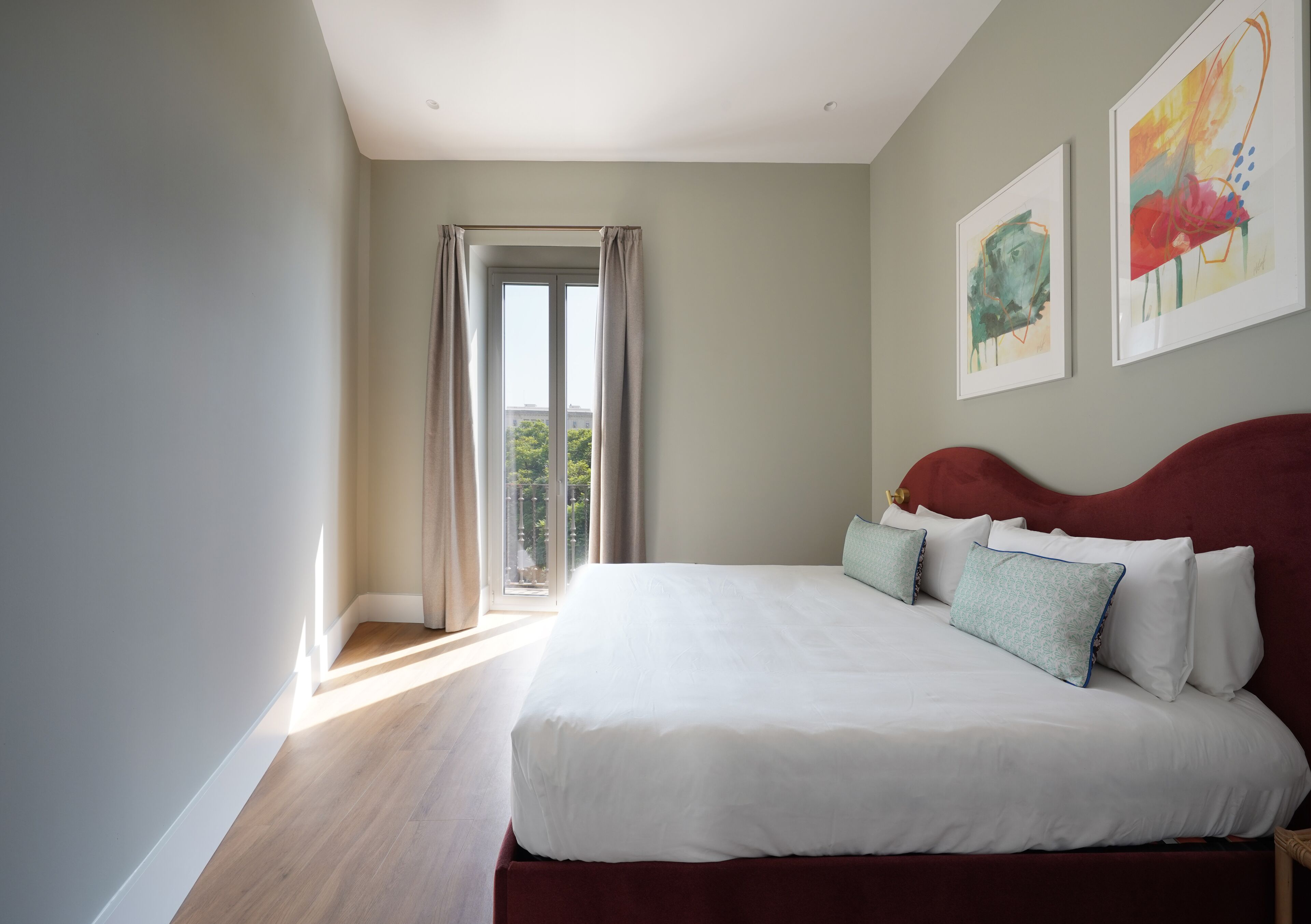 A bedroom with a large bed, a view through an open door, and two framed artworks on the wall.