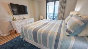 Un dormitorio con cama, televisor, cómoda y balcón.