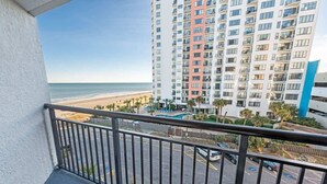 Un balcón con vista a una playa, un estacionamiento y un edificio de gran altura con múltiples balcones.