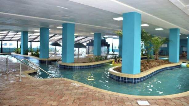 Una piscina interior con bordes de azulejos azules, rodeada de suelo de ladrillo y sostenida por pilares azules.