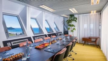 A conference room with a long table, chairs, and a view of the sea through large windows.