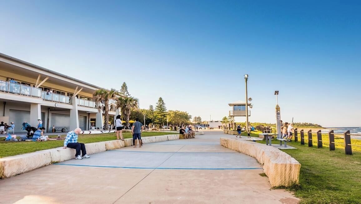 A coastal promenade with a building featuring balconies, a clear sky, and a view of the sea.