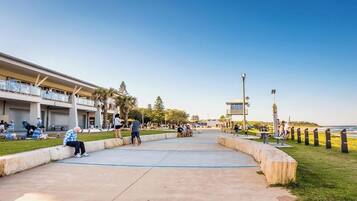 A coastal promenade with a building featuring balconies, a clear sky, and a view of the sea.