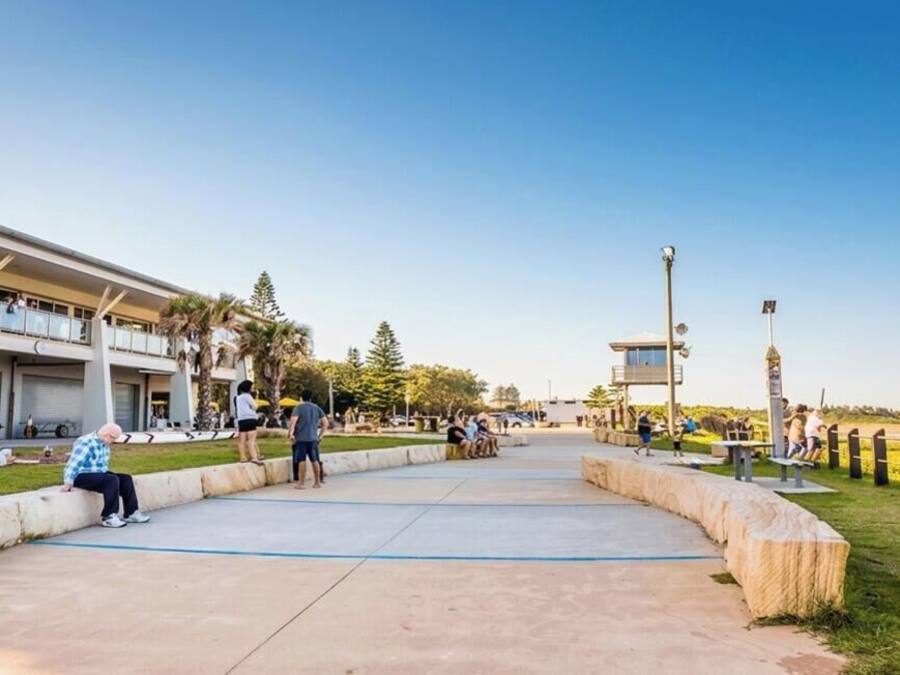 A coastal promenade with a building featuring balconies, a clear sky, and a view of the sea.