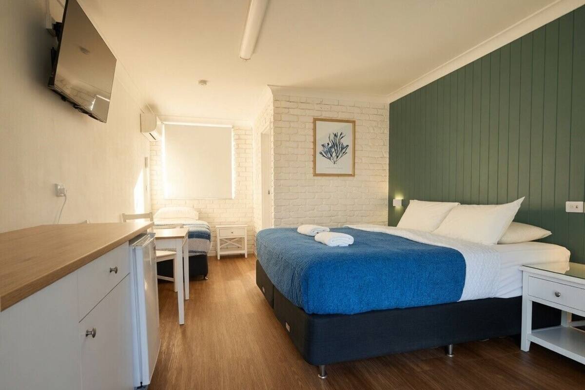 A bedroom with a bed, a desk, a chair, a TV mounted on the wall, and a framed picture on the wall.