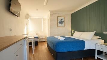 Quarto com uma cama, escrivaninha, cadeira, TV fixada na parede e um quadro enquadrado na parede.