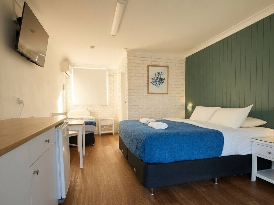Quarto com uma cama, escrivaninha, cadeira, TV fixada na parede e um quadro enquadrado na parede.