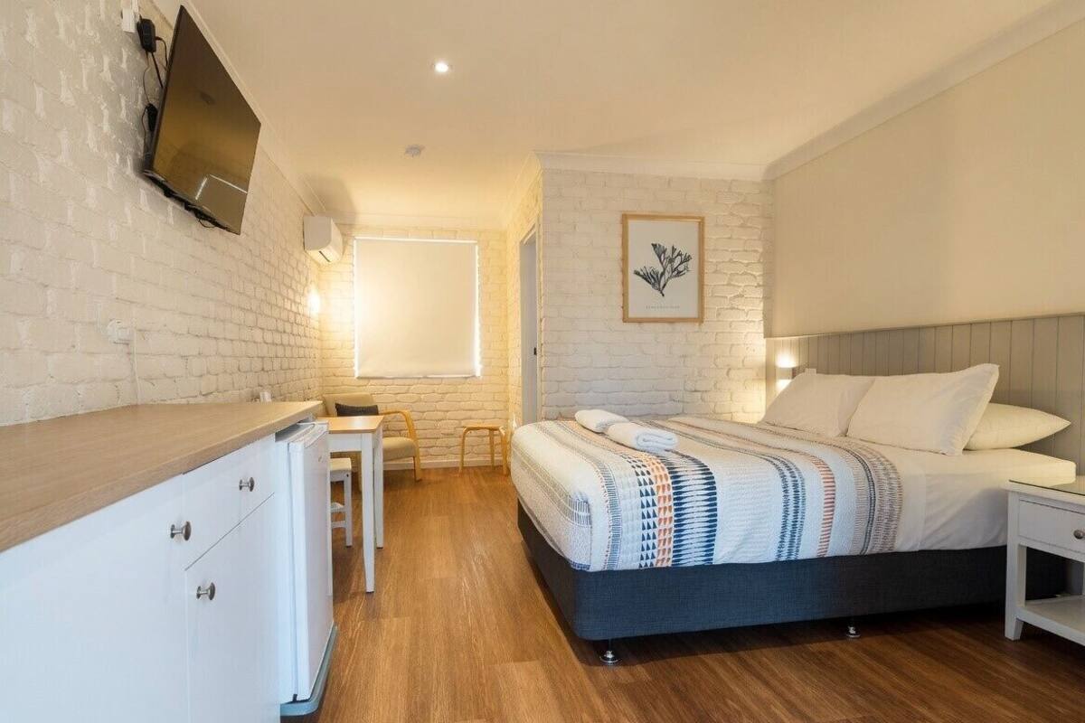 A bedroom with a bed, bedside table, and a desk with a chair.