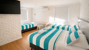 A hotel room with white brick walls, a wooden floor, two beds with striped bedding, a small table, and a TV mounted on the wall. - Bay House Motel (Bateau Bay)
