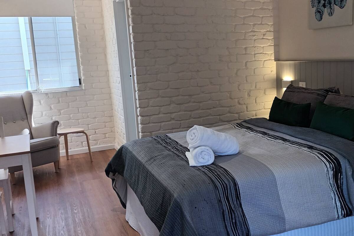 A bedroom with a bed, a bedside table, a chair, and a desk.