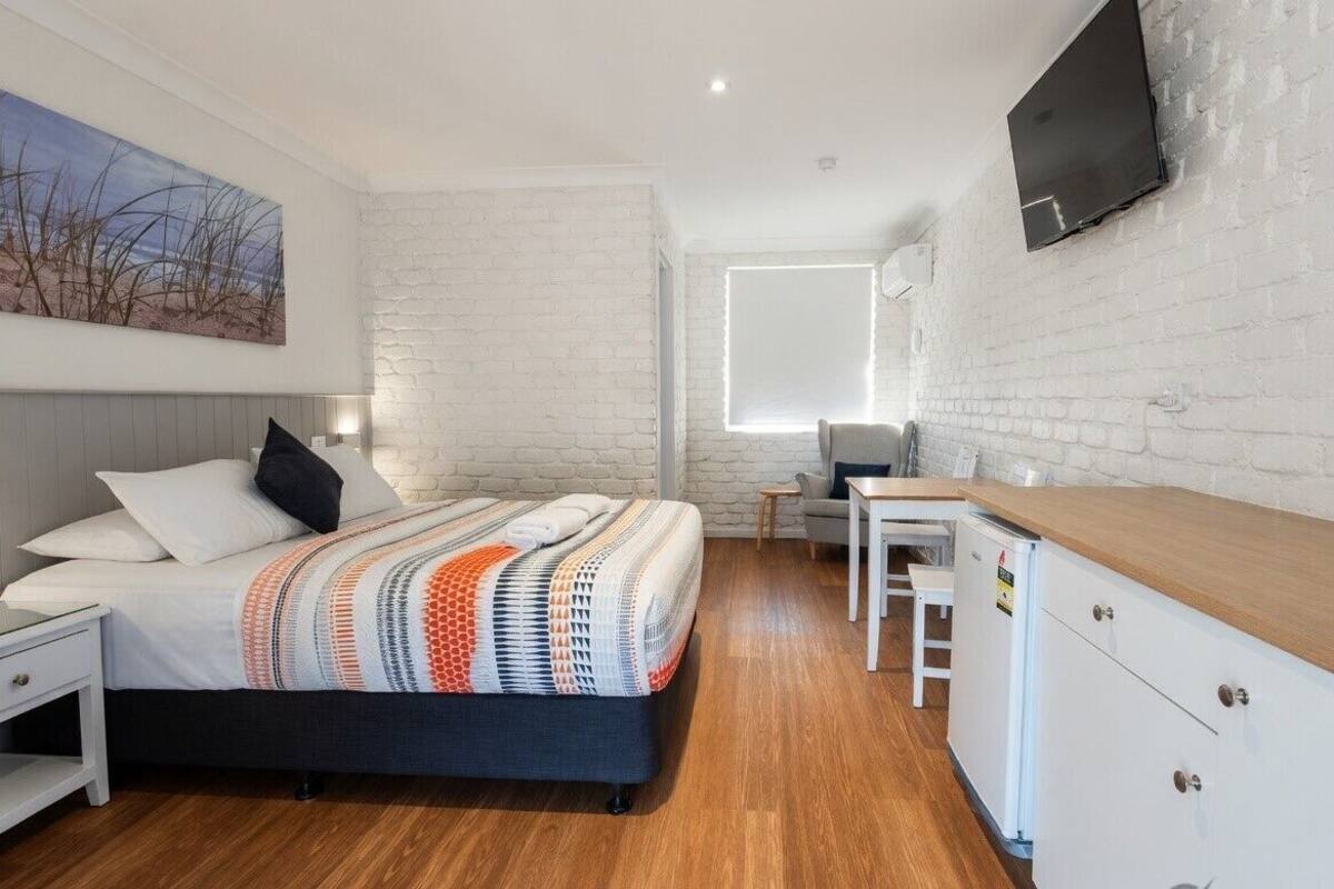 A modern bedroom with a bed, bedside table, and a TV mounted on a brick wall.