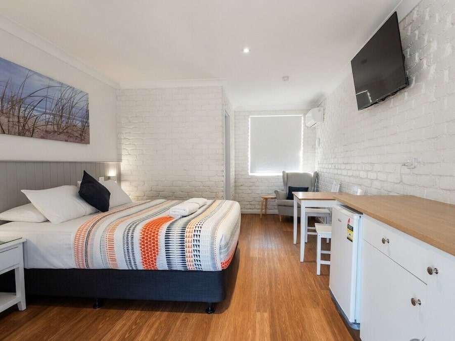 Een moderne slaapkamer met een bed, nachtkastje en een televisie die aan een bakstenen muur is bevestigd.