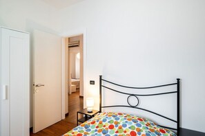 Une chambre à coucher avec un lit, une porte, une table de chevet avec une lampe, et un couloir menant à une autre pièce.