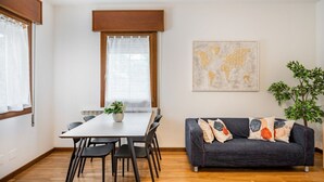 Ein Essbereich mit Tisch und Stühlen, einer Couch mit Kissen, einer Pflanze und einem Wandbild einer Weltkarte.