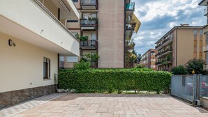 Ein Innenhof mit Hecke, Fliesenboden und mehrstöckigen Gebäuden mit Balkonen.