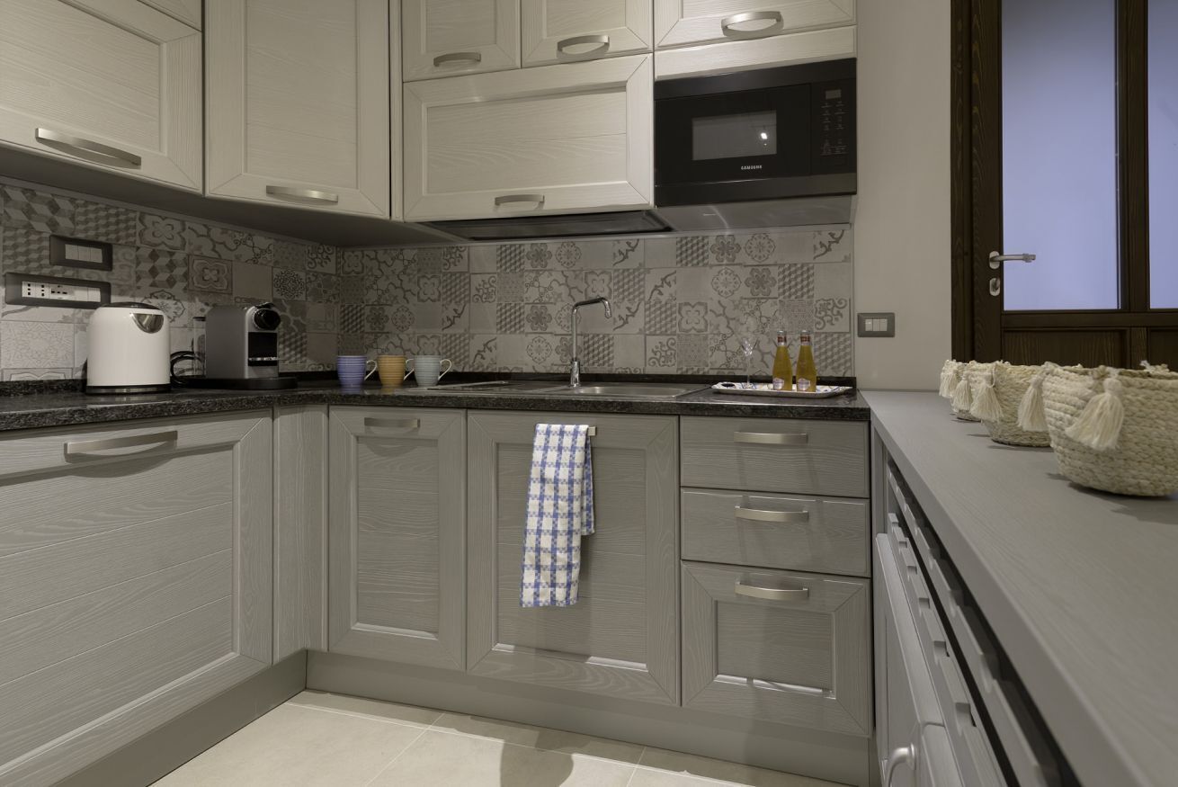 A modern kitchen with grey cabinetry, a microwave, a kettle, and a patterned backsplash.