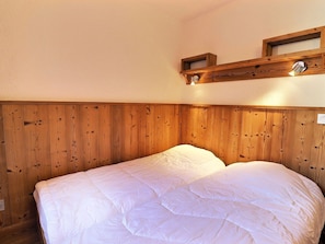 Un lit simple avec une tête de lit en bois et une petite étagère au-dessus.
