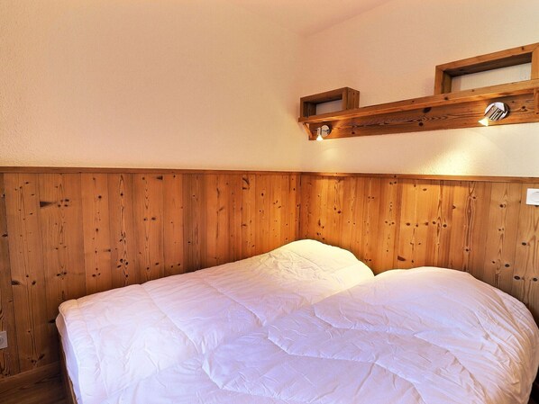 Una cama individual con cabecera de madera y una pequeña estantería arriba.