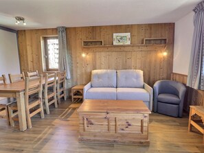Una habitación con paneles de madera, un sofá, una mesa de comedor con sillas, una pequeña mesa de centro de madera y un sillón azul.