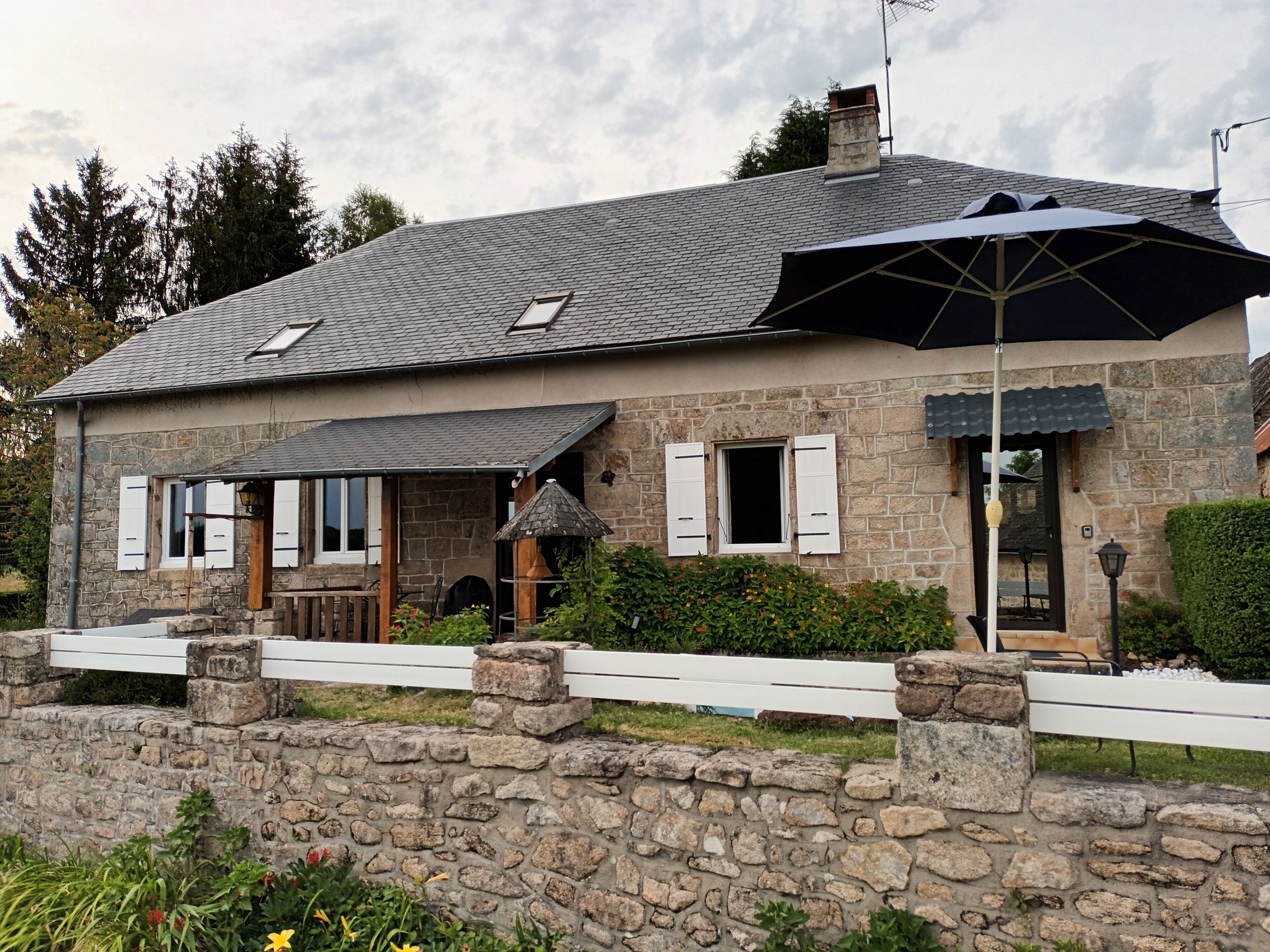 Une maison en pierre avec un toit en pente, une véranda et un mur de pierre à l’avant.