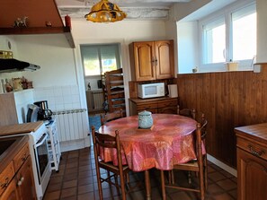 A kitchen with wooden cabinets, a microwave, a stove, and a dining table with chairs. - Maison de Campagne Dans un Petit Village Corrézien (Saint-Priest-de-Gimel)