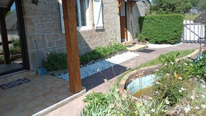 A stone building with a wooden porch, a small garden with a pond, and a metal gate.