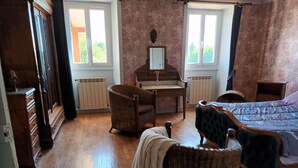 A room with a piano, a wicker chair, a bed, and a dresser.