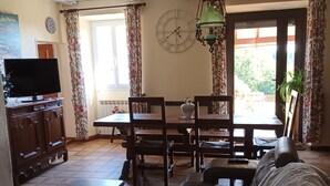 A living room with a sofa, a TV, a dining table, and a clock on the wall.