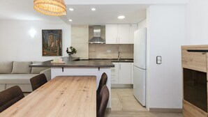 Une cuisine moderne avec des meubles blancs, une table à manger en bois et un luminaire suspendu.