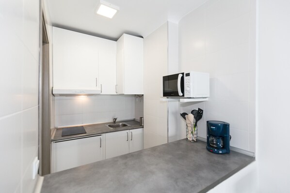 A compact kitchen with white cabinets, a microwave, a coffee maker, and a sink.