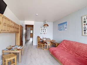 Een knus ingerichte kamer met een rode bank, houten meubels, een eettafel en een wand met foto's.