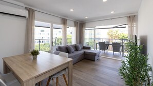 Un saló modern amb taula de dinar de fusta, sofà modular gris i un balcó amb mobles de jardí.