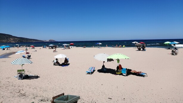 Uma praia com pessoas se banhando ao sol e relaxando sob guarda-sóis.