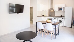 Una cuina moderna amb armaris blancs, microones, rentadora i zona de dinar amb taula i cadires.