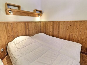 Ein Einzelbett mit weißer Decke in einem Zimmer mit Holzvertäfelung und einem hölzernen Kopfstück.