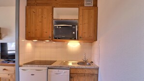 A compact kitchen with wooden cabinets, a built-in microwave, a dishwasher, and a sink. - Comfortable 2-Room with Balcony, Pets Allowed, Ski-in/Ski-out (La Tania)