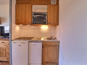 A compact kitchen with wooden cabinets, a built-in microwave, a dishwasher, and a sink.