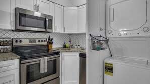 A kitchen with white cabinets, a stainless steel microwave, a stove, a dishwasher, and a washing machine.
