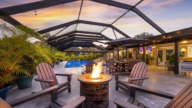 An outdoor seating area with Adirondack chairs, a central fire pit, and a pool in the background.