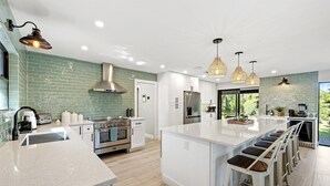 A modern kitchen with white cabinetry, a central island with bar stools, stainless steel appliances, and a green-tiled backsplash.