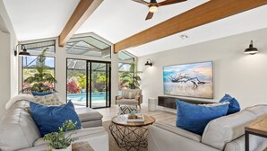 A modern living room with a glass door leading to a pool area, a ceiling fan, and a large painting on the wall.