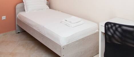 A small, modern bedroom with a single bed, a desk, and a wall clock.