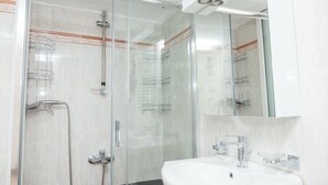 Een moderne badkamer met een douche met glazen wand, een witte wastafel en een grote spiegel.