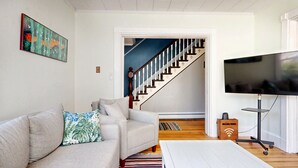 A living room with a sofa, a television, a wooden floor, a staircase, and a painting on the wall. - Dancing Queen by Bayley Vacation Rentals (Old Orchard Beach)