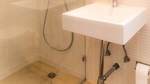Ein Badezimmer mit einem weißen Waschbecken, einer Dusche mit Glastür und einem Spiegel mit aufwendiger Rahmung.