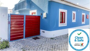 Ein blaues Gebäude mit roter Garagentür, einem Ziegeldach und einem Schild, das 'Clean & Safe' Tourismus in Portugal kennzeichnet.